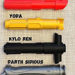 K&ouml;nnte beinhalten: Vier Spielzeug-Lichtschwerter, eines rot, eines gelb, eines schwarz und eines grau, mit den Namen Darth Vader, Yoda, Kylo Ren und Darth Sidious, die &uuml;ber jedem gedruckt sind.