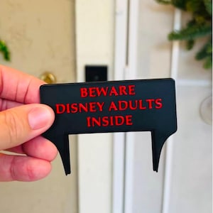 May include: Black sign with red text that reads "Beware Disney Adults Inside".