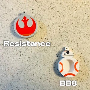 May include: Two round, white, 3D printed ornaments. The first ornament features the red Rebel Alliance symbol with the text "Resistance". The second ornament features a white and orange BB-8 character with the text "BB8".
