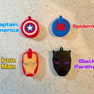May include: Four different superhero character keychains. The keychains are made of plastic and feature the characters Captain America, Spiderman, Iron Man, and Black Panther. The keychains are all in different colors and have different designs.