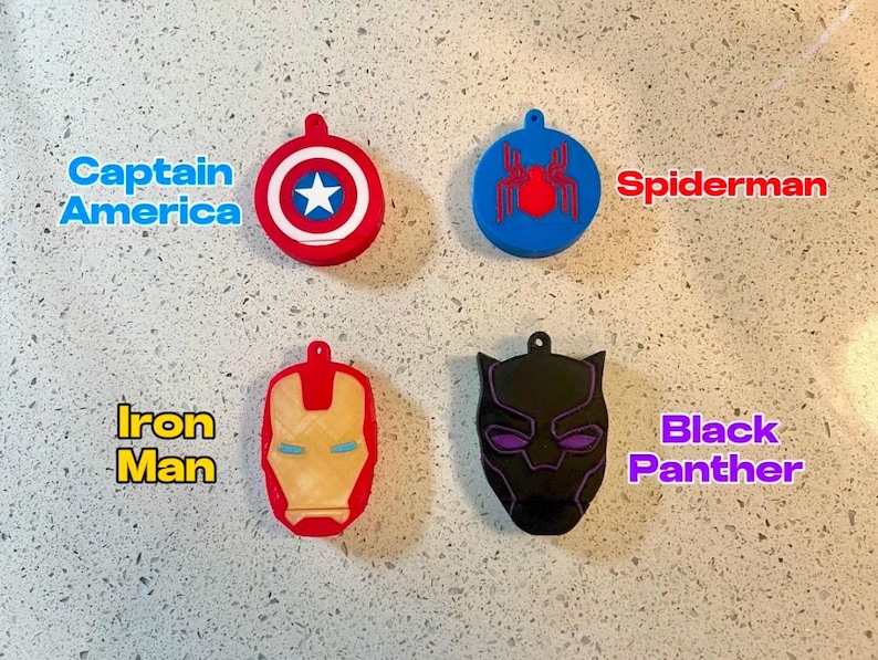May include: Four different superhero character keychains. The keychains are made of plastic and feature the characters Captain America, Spiderman, Iron Man, and Black Panther. The keychains are all in different colors and have different designs.