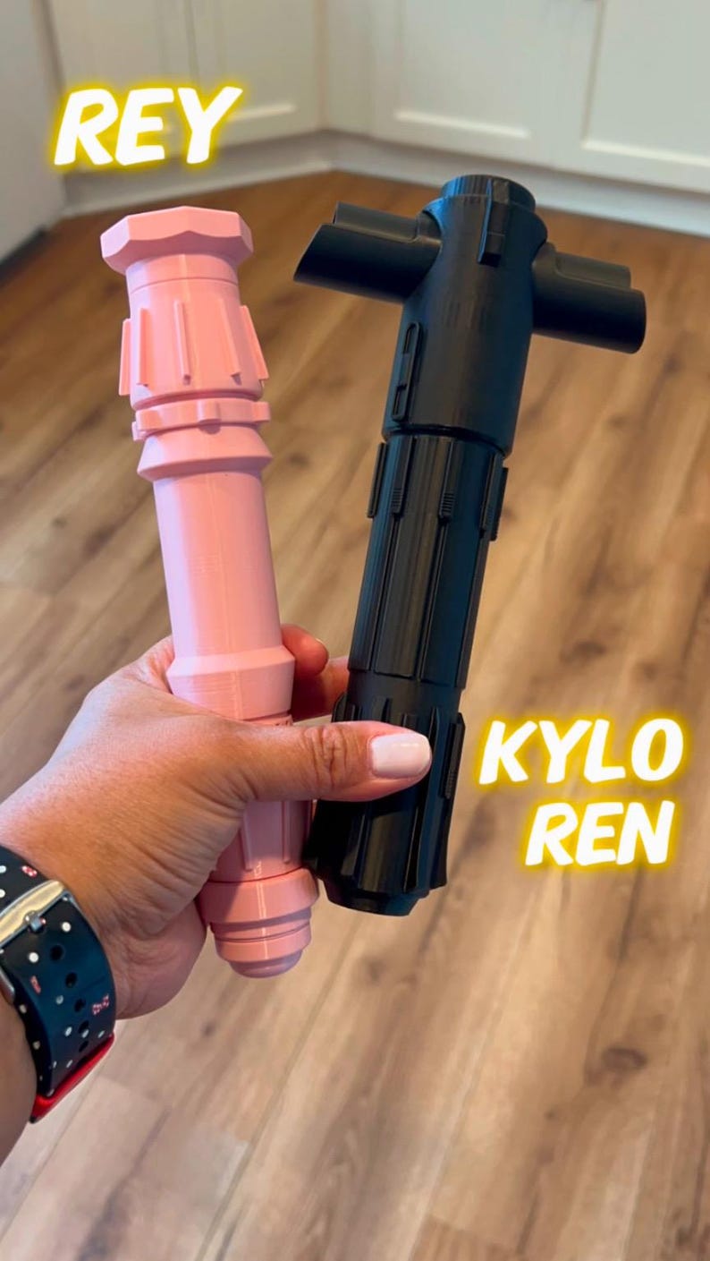 K&ouml;nnte beinhalten: Zwei Lichtschwert-Requisiten, eine rosa und eine schwarze, mit den Worten "REY" und "KYLO REN" darauf.