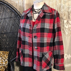 May include: A red, black, and grey plaid jacket with a collared neckline, two front pockets, and three large buttons. The jacket is displayed on a mannequin with a black beaded necklace and a red top underneath.