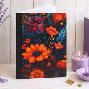 May include: A notebook with a black spine and a front cover featuring a vibrant floral pattern of bright orange, deep red, and dark purple flowers against a dark, textured background. The notebook is open slightly, revealing white lined pages.