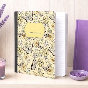 May include: A notebook with a pale yellow cover featuring a repeating pattern of black-outlined butterflies, flowers, and small stars. A central blank label with a dotted line is present. The notebook has a black spine and white lined pages.