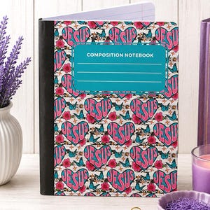 May include: A composition notebook with a black spine and a white cover featuring a repeating pattern of pink hearts containing the word JESUS in blue, interspersed with blue butterflies, pink flowers, and small stars, plus a teal label with text.