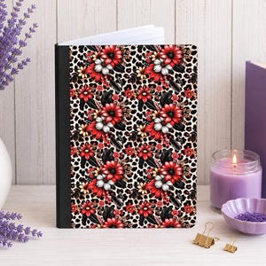 May include: A notebook with a black spine and a cover featuring a repeating pattern of red and white flowers layered over a black and tan leopard print background. The notebook is shown with white lined paper visible at the top edge of the cover.