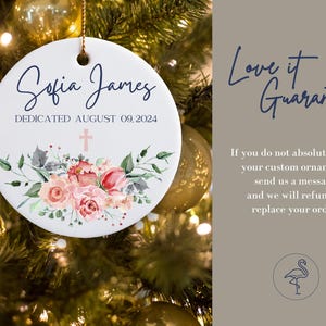 May include: White ceramic Christmas ornament with a pink floral design and a cross. The ornament is personalized with the text "Sofia James Dedicated August 09, 2024".