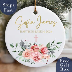 May include: White ceramic ornament with gold lettering that reads "Sofia James Baptized June 14, 2024". The ornament is decorated with a pink cross and watercolor floral design.