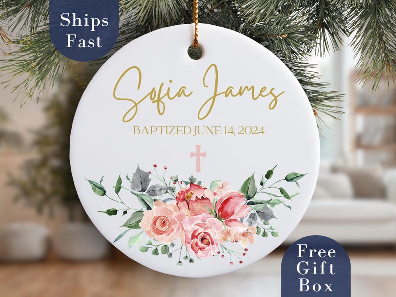 May include: White ceramic ornament with gold lettering that reads "Sofia James Baptized June 14, 2024". The ornament is decorated with a pink cross and watercolor floral design.