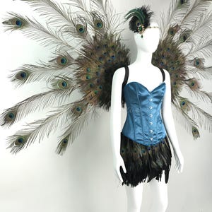 May include: A teal satin corset with a front hook closure, paired with a black feather skirt and large, expansive peacock feather wings. A matching headpiece features a dark green jewel and black feathers, completing the ensemble.