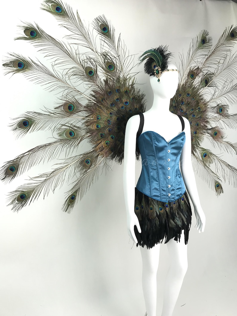 May include: A teal satin corset with a front hook closure, paired with a black feather skirt and large, expansive peacock feather wings. A matching headpiece features a dark green jewel and black feathers, completing the ensemble.