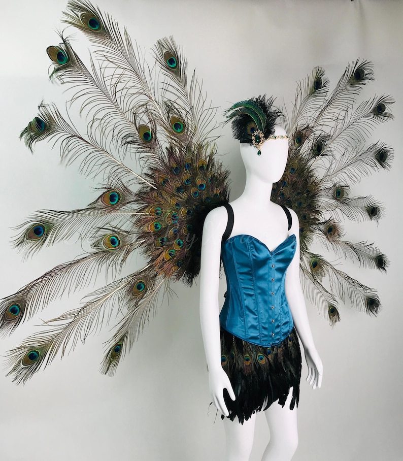 May include: A costume set featuring large, expansive wings constructed from iridescent peacock feathers, paired with a teal satin corset and a black feathered skirt. A matching peacock feather headpiece with a central green jewel is included.