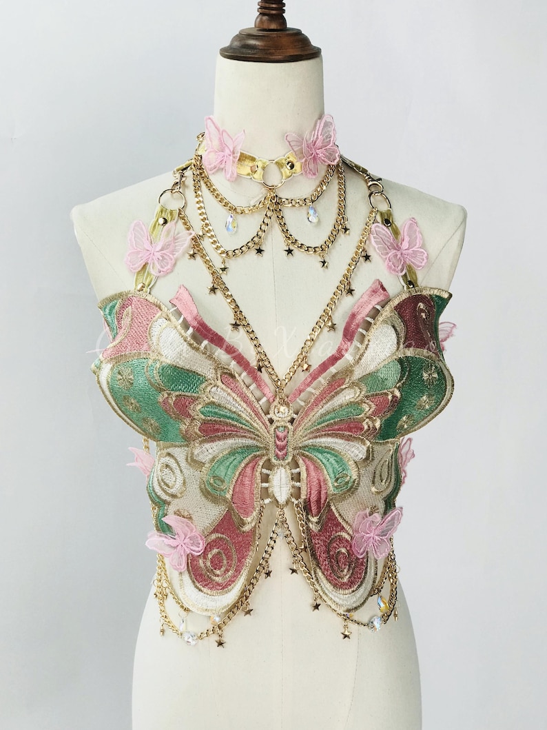 May include: A butterfly-shaped bodice with gold chain accents and pink butterfly embellishments. The bodice features embroidered details in shades of green, pink, and white. A matching choker necklace with pink butterflies and gold chain completes the look.