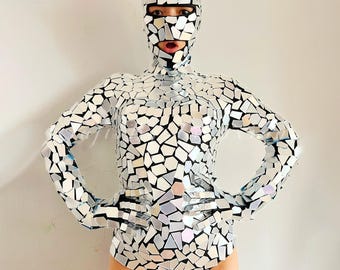 May include: A silver bodysuit with a mirrored mosaic pattern. The bodysuit has long sleeves and a high neck. The person wearing the bodysuit is also wearing a silver mirrored mask.