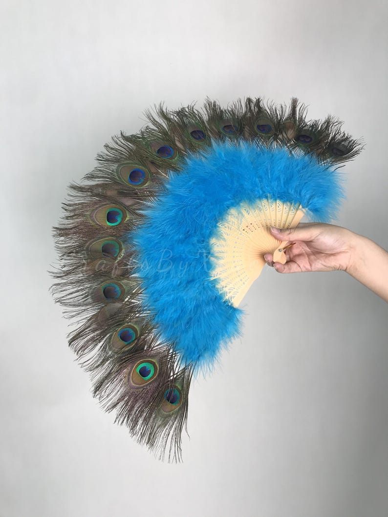 May include: A hand fan featuring a light wood frame and a vibrant blue feather center, bordered by a row of natural peacock feathers with distinct iridescent eye patterns. The fan is fully extended, showcasing the contrast between the bright blue plumage.