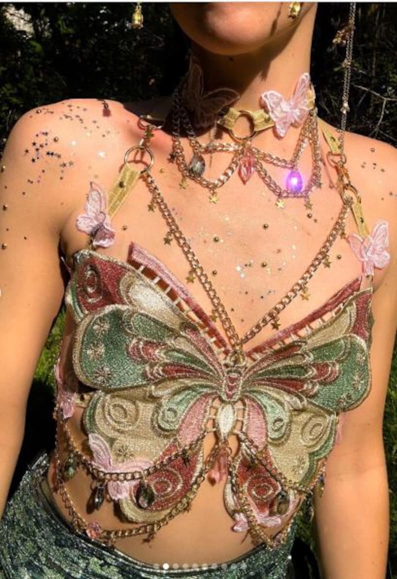 May include: A butterfly-themed top with gold chain accents. The top features an embroidered butterfly design in shades of green, pink, and gold. Additional details include a matching choker and decorative chains with star and gem pendants.