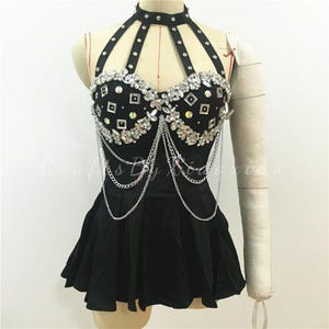 Op de afbeelding: Zwarte haltertop met een hoge halslijn en een uitlopende rok. De bustier is versierd met strass-steentjes en zilveren kettingen. De top wordt op een mannequin getoond.
