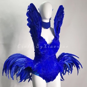 Puede incluir: Un disfraz de plumas azul con un corpiño, alas y una falda. El disfraz está hecho de plumas azules y tiene un escote de corazón.