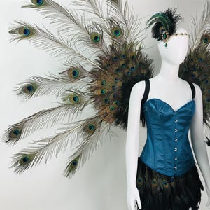 May include: A teal corset top paired with a black feather skirt and large peacock feather wings. The ensemble includes a matching headpiece featuring a green jewel and black feathers, worn on a white mannequin to display the full costume design.