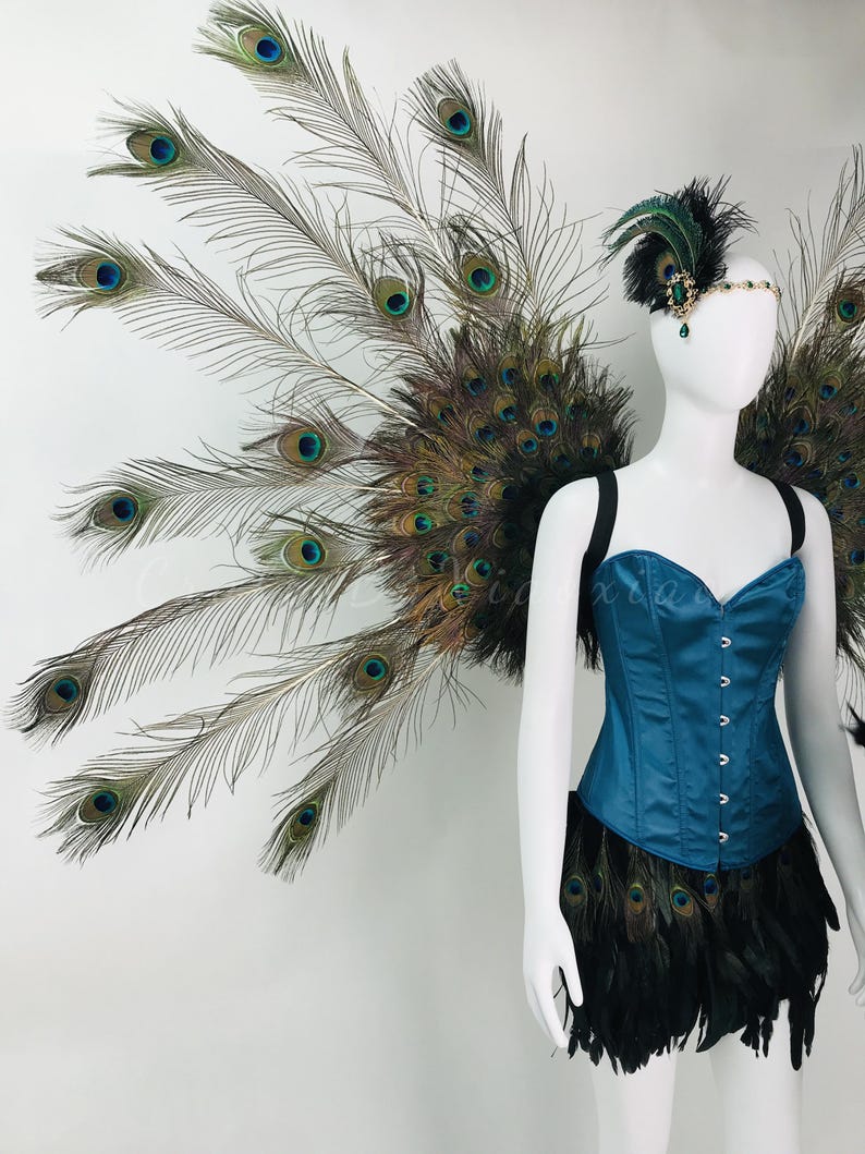 May include: A teal corset top paired with a black feather skirt and large peacock feather wings. The ensemble includes a matching headpiece featuring a green jewel and black feathers, worn on a white mannequin to display the full costume design.