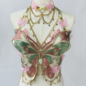 May include: A decorative butterfly-shaped bodice with a matching choker. The bodice features intricate embroidery in shades of pink, green, and gold, with delicate butterfly accents and dangling chains. The choker and chains are gold-toned.
