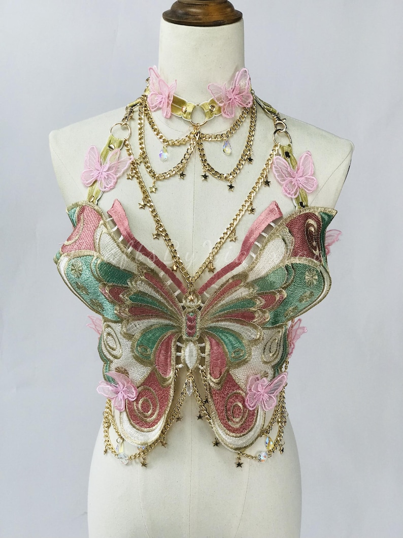 May include: A decorative butterfly-shaped bodice with a matching choker. The bodice features intricate embroidery in shades of pink, green, and gold, with delicate butterfly accents and dangling chains. The choker and chains are gold-toned.