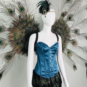 May include: A teal satin corset with a front hook closure, paired with a black feather skirt and large peacock feather wings. A matching headpiece features a green gemstone, black feathers, and a gold-toned chain across the forehead.