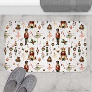 May include: A rectangular bath mat featuring a repeating Christmas pattern on a white background. The design includes illustrations of nutcracker soldiers, ballerinas, mice in royal attire, candy canes, holly sprigs, and holiday ornaments.