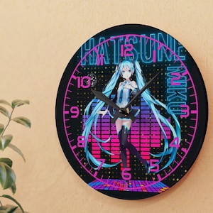 May include: A round black wall clock featuring a colorful anime character with long blue hair. The clock face has the words "HATSUNE MIKU" in pink and blue neon-style lettering. The clock hands are black.