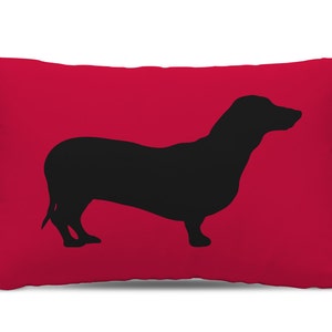 May include: Red throw pillow with a black silhouette of a dachshund.