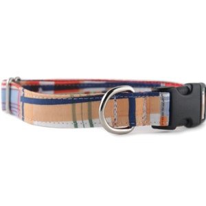 May include: A patterned dog collar with a black plastic buckle and a silver metal D-ring. The collar is made of a fabric with a plaid pattern in shades of blue, red, and beige.