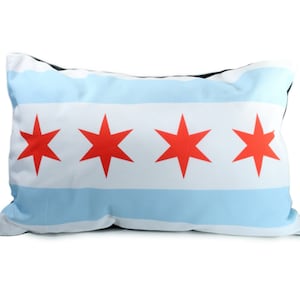 May include: Rectangular cushion featuring the Chicago city flag design. The cushion has a white background with two light blue horizontal stripes and four red six-pointed stars. The cushion's edges are black.