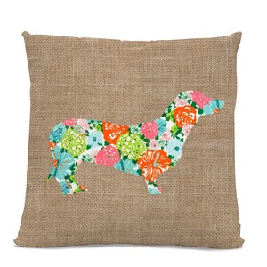 May include: A brown burlap pillow with a floral dachshund silhouette. The dachshund is made of a fabric with a bright floral pattern in shades of pink, orange, green, and blue.