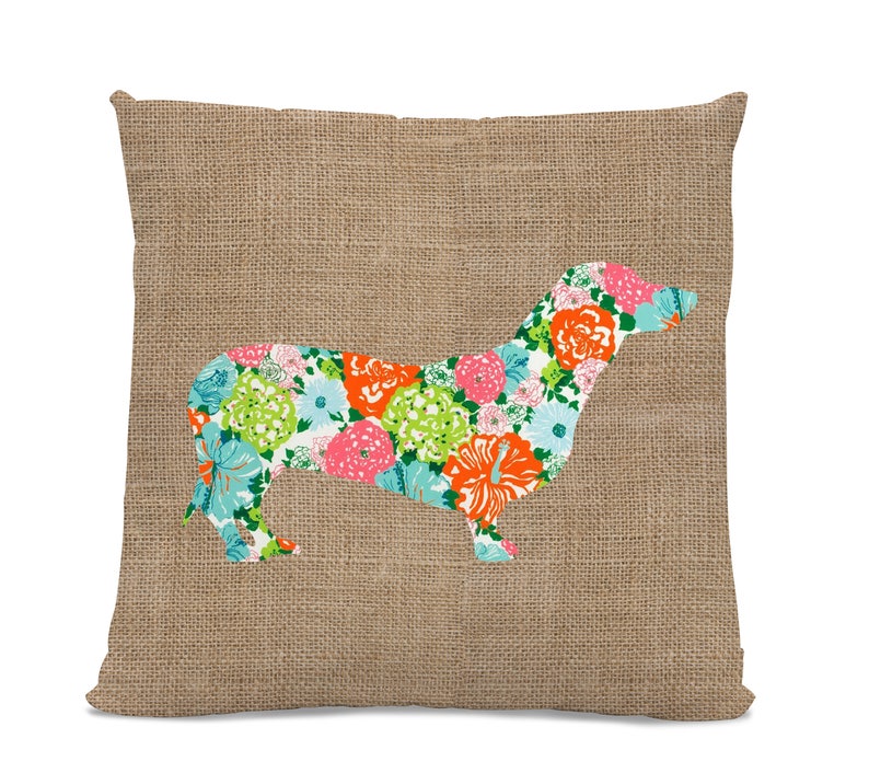May include: A brown burlap pillow with a floral dachshund silhouette. The dachshund is made of a fabric with a bright floral pattern in shades of pink, orange, green, and blue.
