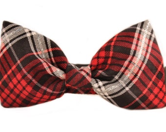 May include: A red, black, and white plaid bow tie with silver accents. The bow tie is adjustable and has a black strap.