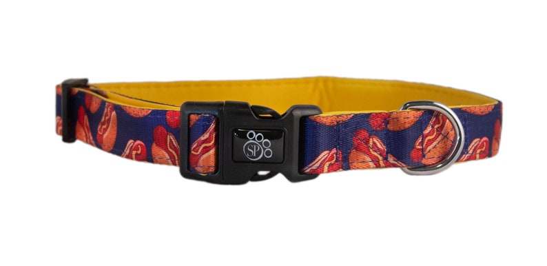 May include: A blue and yellow dog collar with a hot dog print. The collar has a black buckle with a paw print logo and a silver D-ring.