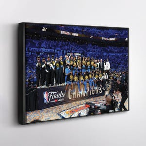 May include: A framed photograph captures a team celebrating a championship victory. The team is wearing black and gold uniforms, holding a trophy, and standing on a stage with a banner that reads "Finals Champions". Confetti fills the air.