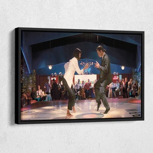 May include: A black and white framed print of a scene from the movie Pulp Fiction. Two people are dancing on a circular dance floor with a clock face design. The woman is wearing a white jacket and black pants. The man is wearing a black suit. The background is a dimly lit bar with people sitting at tables.