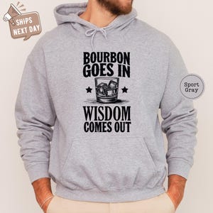 a man wearing a grey hoodie that says bourbon goes in wisdom comes out