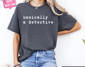 May include: A dark heather grey t-shirt with the text "basically a detective" printed in white.