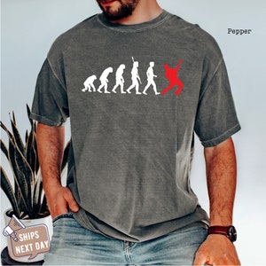 May include: A gray t-shirt with a white silhouette of the evolution of man, ending with a red silhouette of a person playing a guitar. The text "Pepper" is in the top right corner of the image.