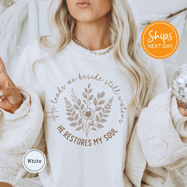 A woman wearing a white t-shirt with a floral design and text printed on it.