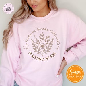 A woman wearing a pink sweatshirt with a floral design and text printed on it.