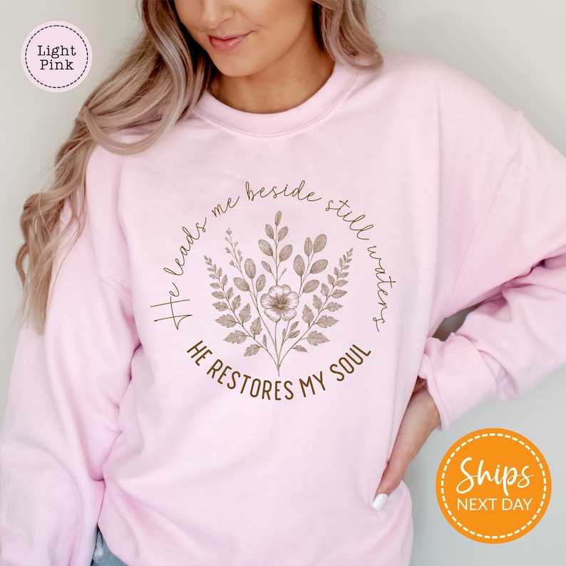 A woman wearing a pink sweatshirt with a floral design and text printed on it.