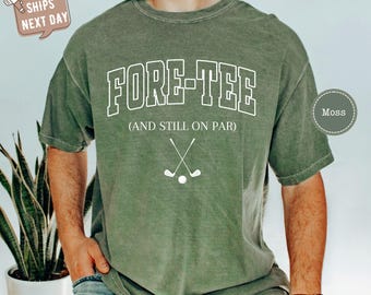 May include: A green t-shirt with the text "FORE-TEE (AND STILL ON PAR)" in white. The shirt features a white graphic of two crossed golf clubs and a golf ball.