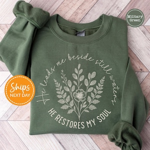 A green sweatshirt with a floral design and text printed on it, laid out on a wooden surface.