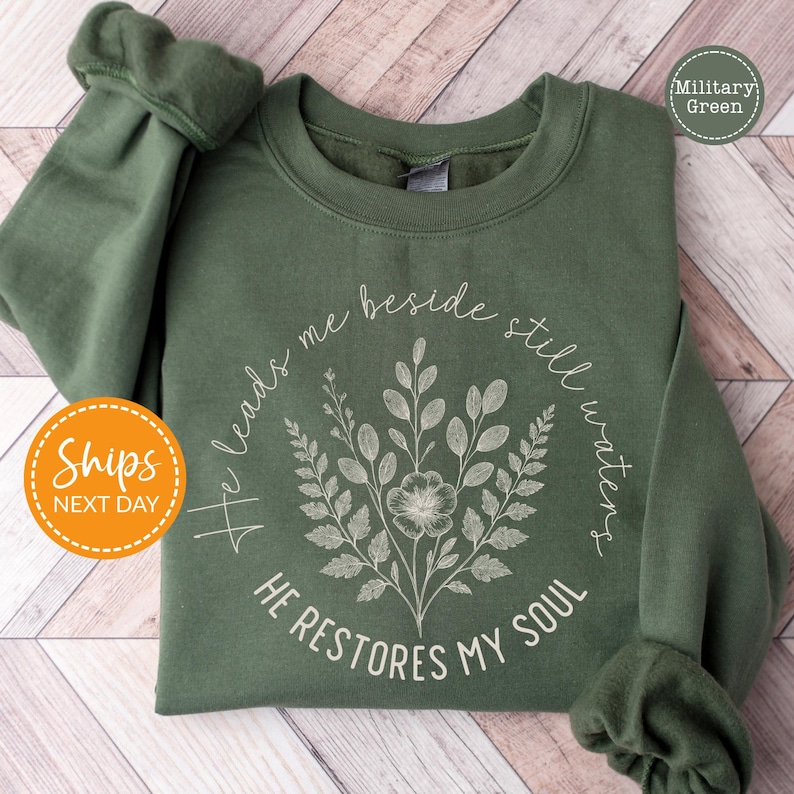 A green sweatshirt with a floral design and text printed on it, laid out on a wooden surface.
