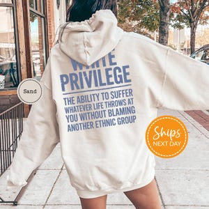 A person wearing a white hoodie with text printed on it, standing on a sidewalk.