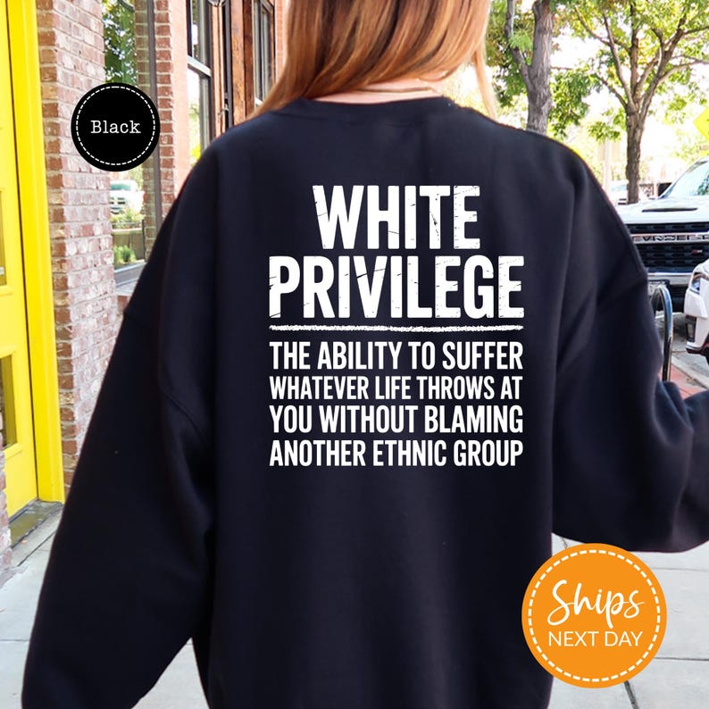 a person wearing a black sweatshirt with white text on the back. The text reads "WHITE PRIVILEGE" and "THE ABLE TO Suffer whatever life throws at YOU without Blaming another Ethnic Group".